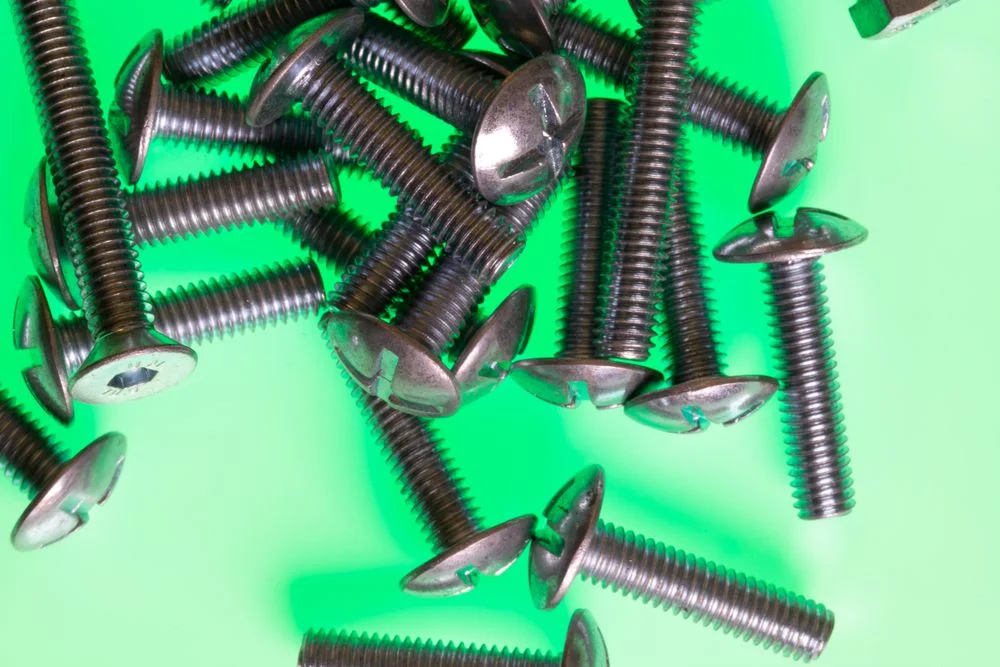 Parafusos de aço inox de diferentes tipos espalhados sobre uma superfície verde vibrante.