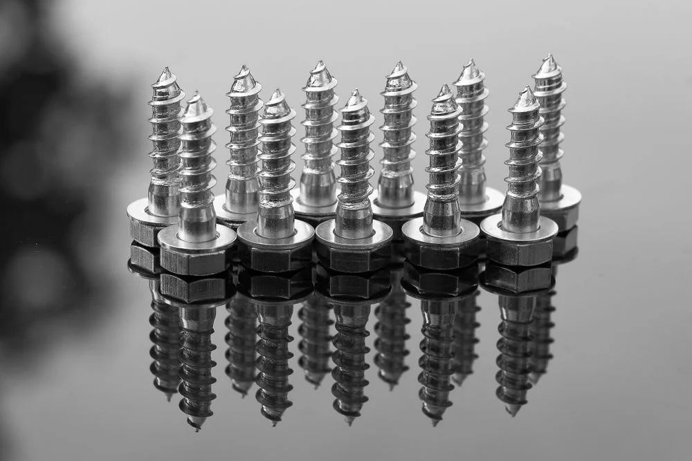 Close-up de parafusos de aço inox 304 e 316 refletindo em uma superfície polida. 