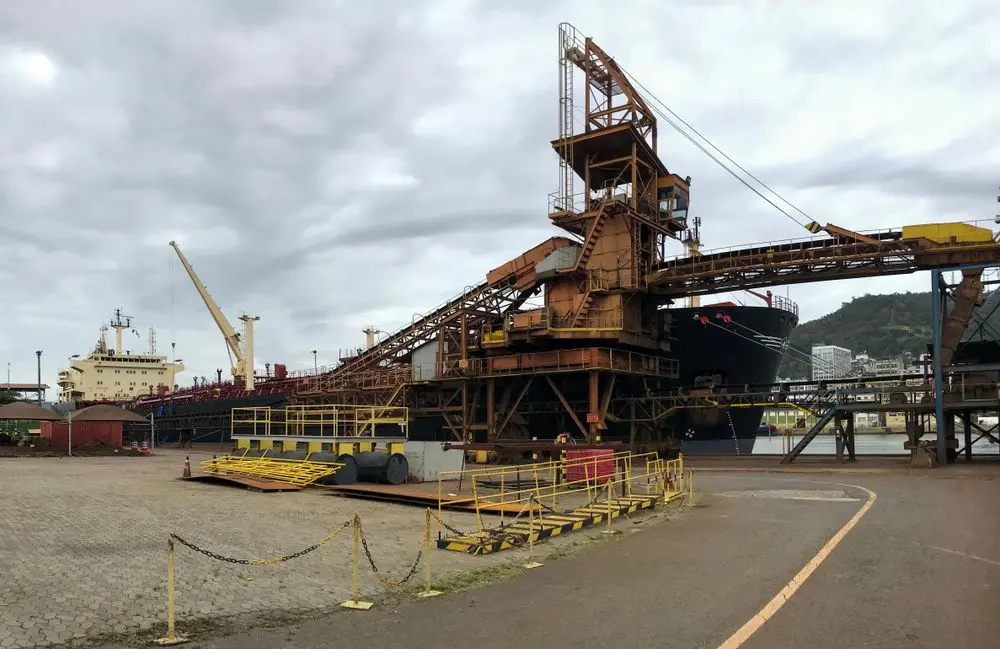 Um porto industrial movimentado com navios, guindastes e um cais de carga sob um céu nublado.